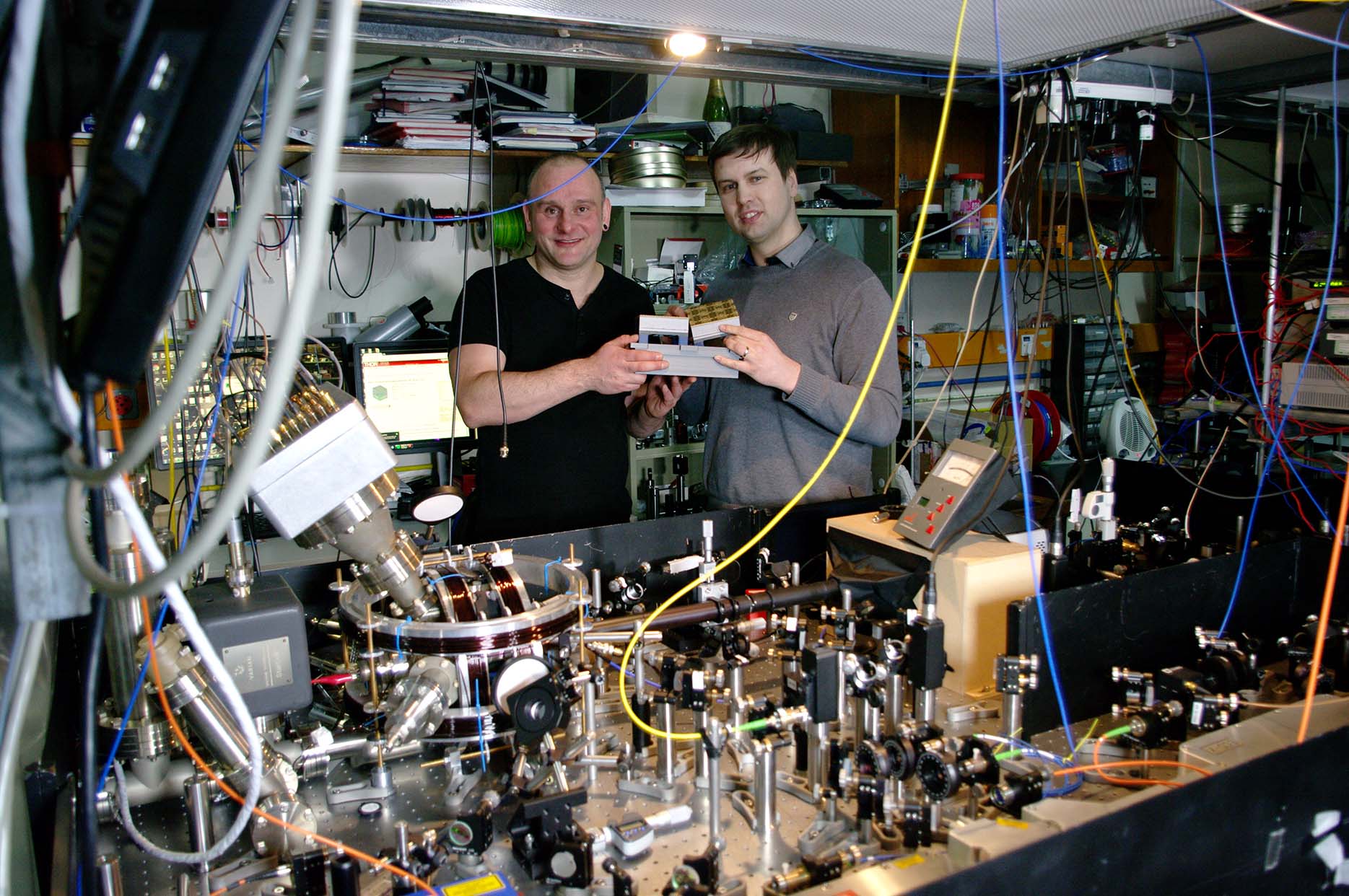 Prof. Hensinger (left) and Dr Lekitsch (right) with a quantum computer blueprint model behind a quantum computer prototype at the University of Sussex. Prof. Hensinger (left) and Dr Lekitsch (right) with a quantum computer blueprint model behind a quantum computer prototype at the University of Sussex.